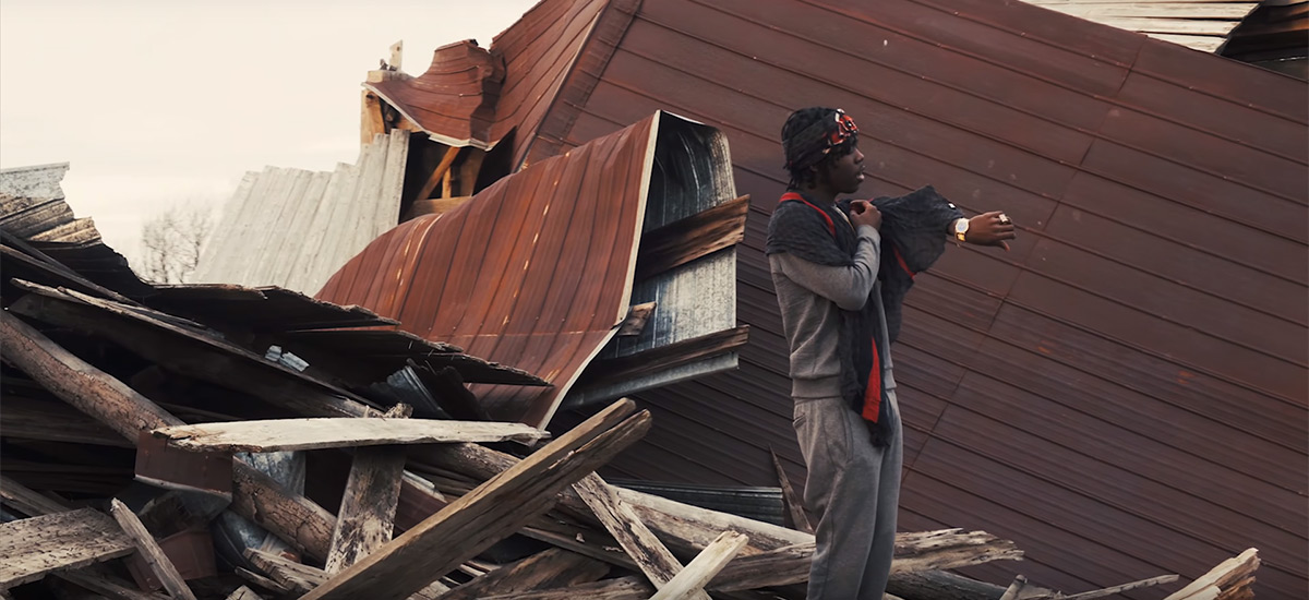 Toronto rapper Burna Bandz checks his gold watch in front of a torn down barn in Beast Mode.