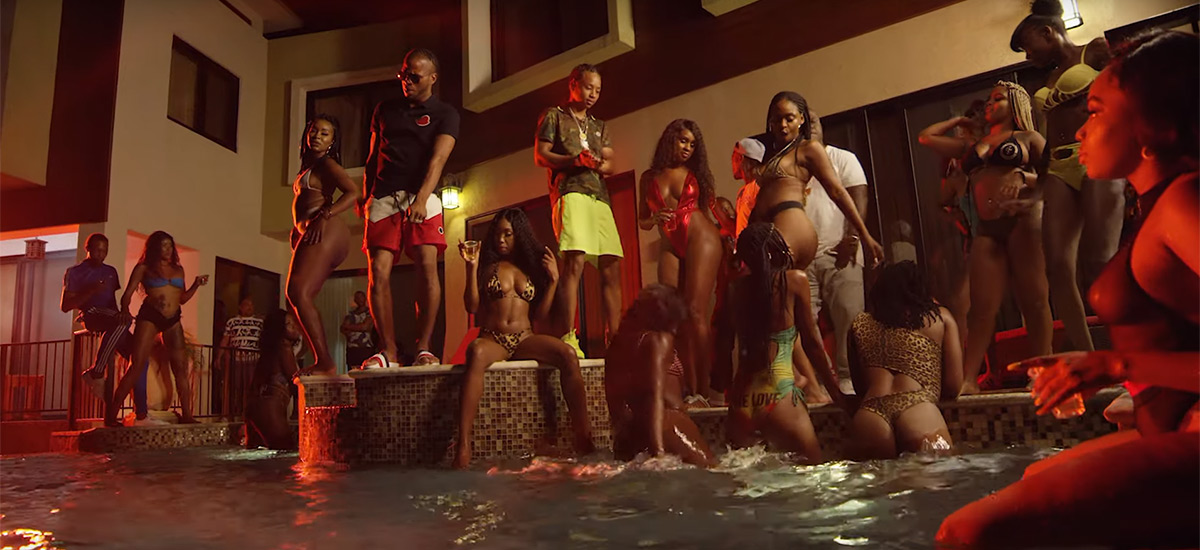 Screenshot from the new Big Accident music video by Pressa and Dexta Daps. The 2 artists are seen partying with a group of women around a pool.