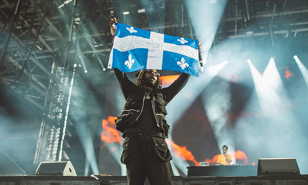 Rapper Jazz Cartier holds up a Quebec flag during his performance on Day 1 of FEQ 2019