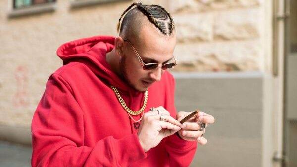 Photo of Vancouver artist Kresnt wearing a red hoodie and sunglasses, while rolling a joint.