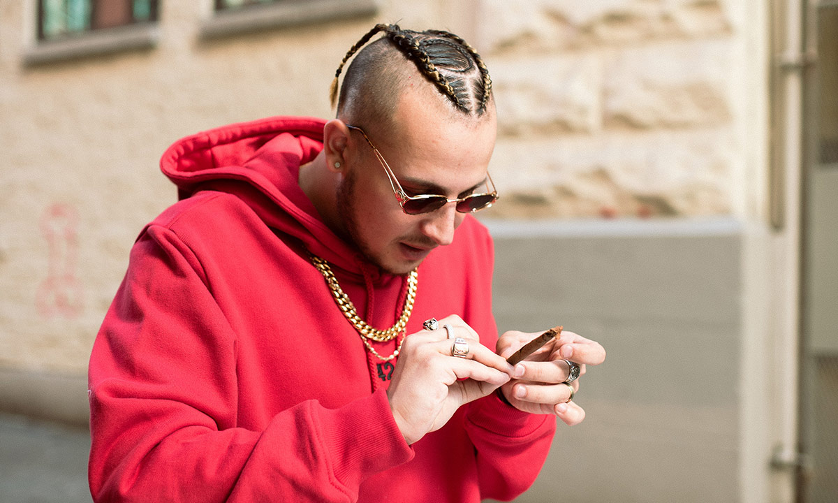 Photo of Vancouver artist Kresnt wearing a red hoodie and sunglasses, while rolling a joint.