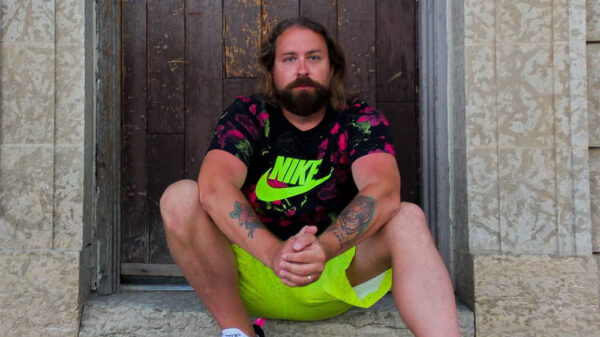 Canadian rapper Fortunato sits on a stoop wearing a black Nike shirt with a fluorescent logo, and matching fluorescent coloured shorts.