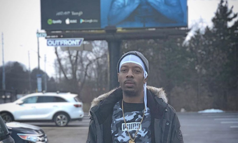 Mezziah standing in front of a Blue Aura billboard advertisement