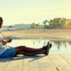 A man sits on a dock and looks at his phone with headphones on.