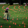 Margot King, age four, touches an orange flag, representing children who died at Indian Residential Schools in Canada, placed in the grass at Major’s Hill Park in Ottawa, on July 1, 2021. (THE CANADIAN PRESS/Justin Tang)