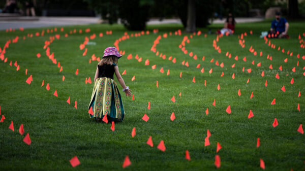 Margot King, age four, touches an orange flag, representing children who died at Indian Residential Schools in Canada, placed in the grass at Major’s Hill Park in Ottawa, on July 1, 2021. (THE CANADIAN PRESS/Justin Tang)