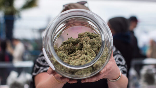 A woman holds up a jar of weed.