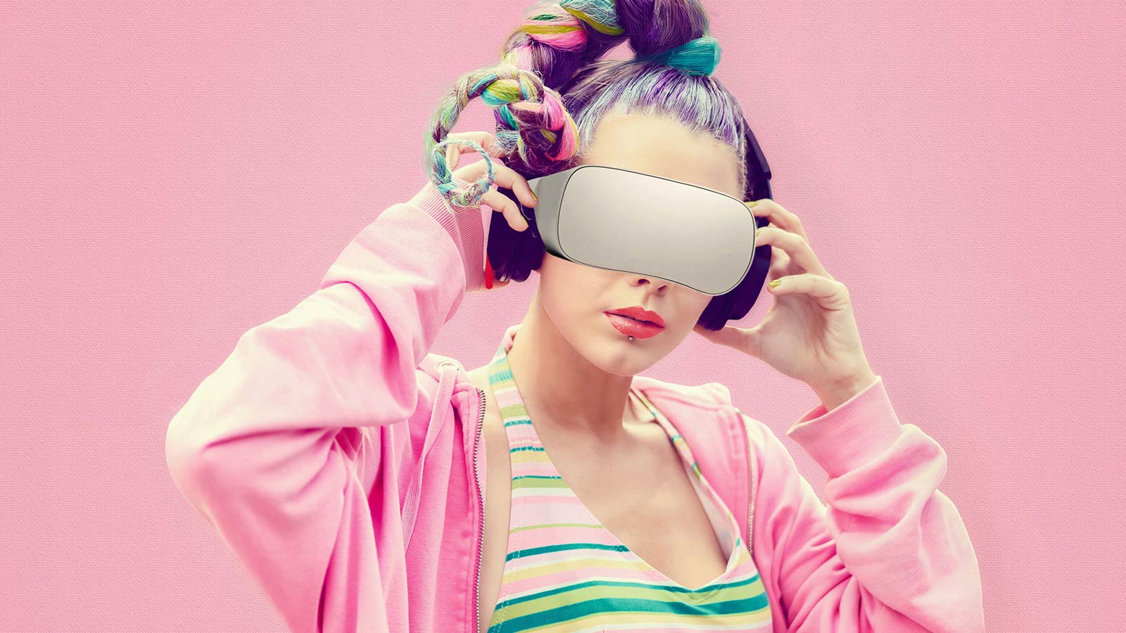 Over a pink background, a young woman with colourful hair wears a virtual reality headset