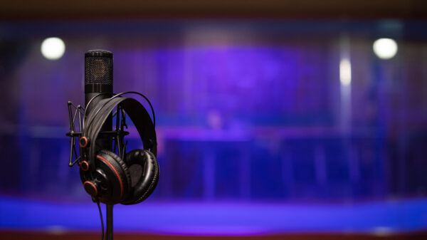 A pair of headphones resting on a microphone stand, with a blue backdrop in what appears to be a recording studio