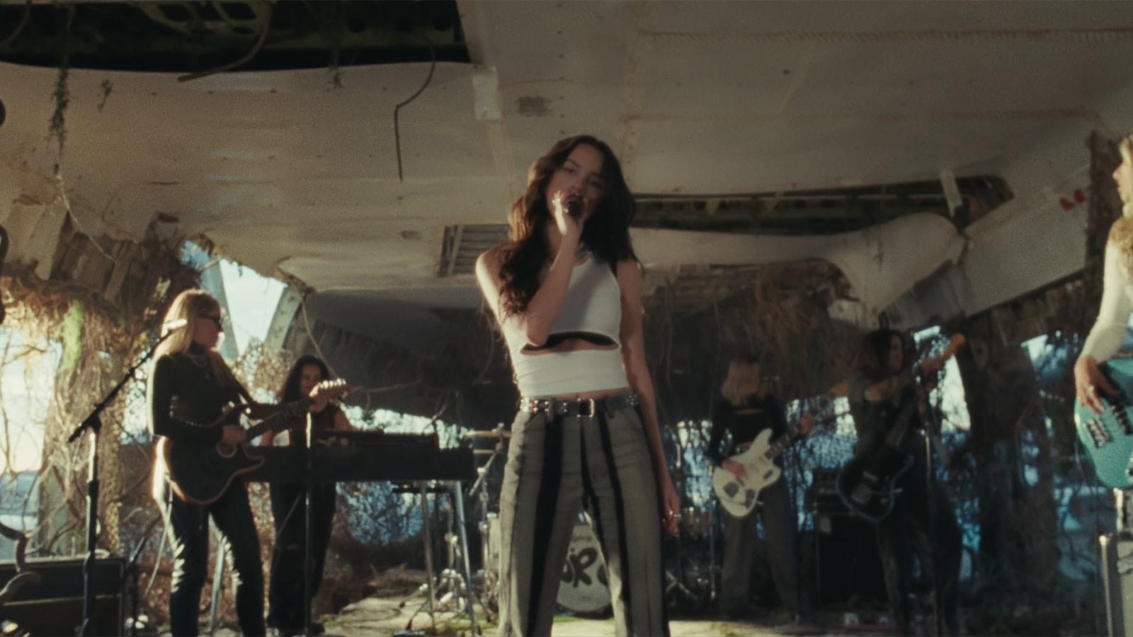 Olivia Rodrigo holding a microphone with a band playing behind her