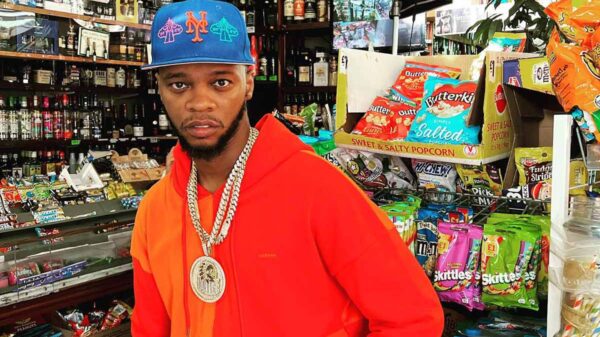 Papoose in a convenience store wearing an orange and red hoodie and a blue hat