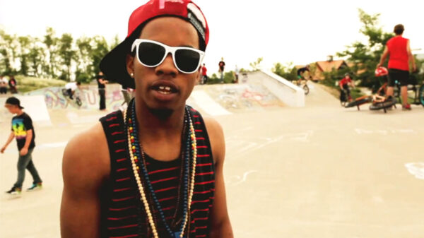 Tory Lanez in the Styll video with a backwards red hat and white sunglasses.