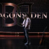 A man and a woman stand side-by-side in front of the Dragons Den logo
