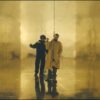 Two men stand in a gold room