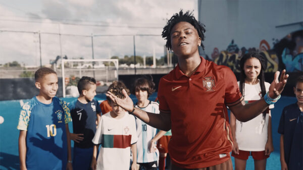A man, IShowSpeed, wearing a soccer jersey and holding his arms out, raps in front of a group of children