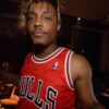 A man with a light dreads and a Chicago Bulls jersey looks at the camera