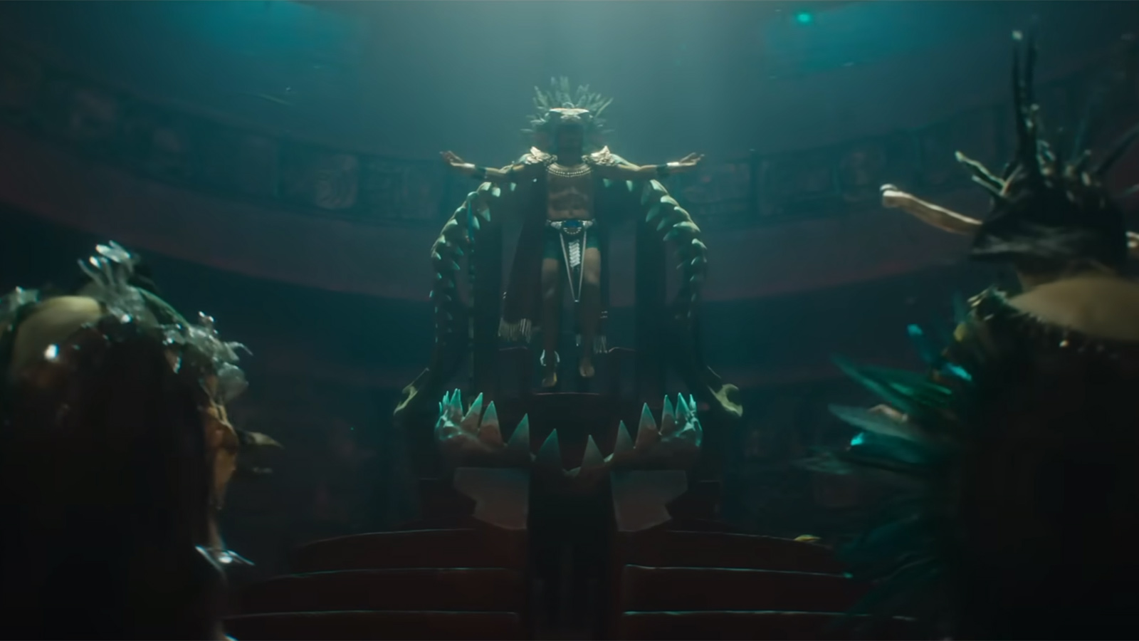 A man named Namor wearing a ceremonial-looking outfit stands on top of a throne.