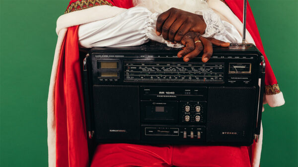 A man in a Santa costume holds a boombox on his lap.