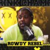 New York rapper Rowdy Rebel sits in a recording studio in front of a mic while wearing headphones.