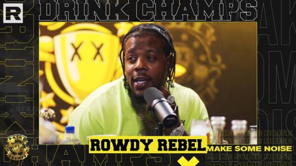New York rapper Rowdy Rebel sits in a recording studio in front of a mic while wearing headphones.