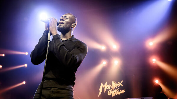 UK star rapper Stormzy holds a mic in both hands while performing on stage.