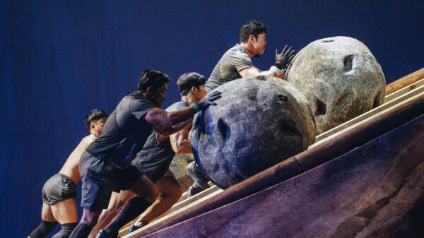 Three men pushing large stone boulders up a hill in a competition.