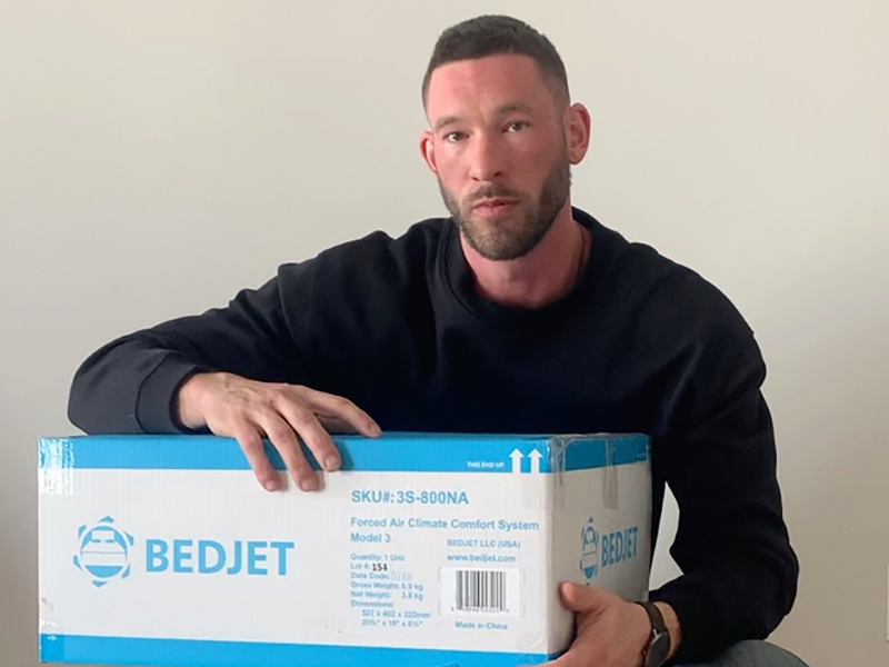 A man looks at the camera while holding a box with the words BedJet written on it