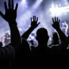 Silhouettes of people at a concert with their hand's raised.