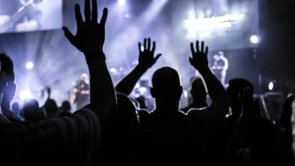 Silhouettes of people at a concert with their hand's raised.