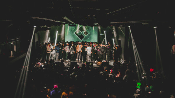 A stage full of people crowd around two people engaging in a rap battle.