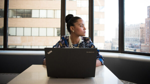A young woman looks out the window while sitting in front of a laptop.