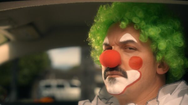 An unhappy looking clown with a red nose and green hair.
