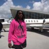 A man in a pink and silver hoodie walks in front of a private jet