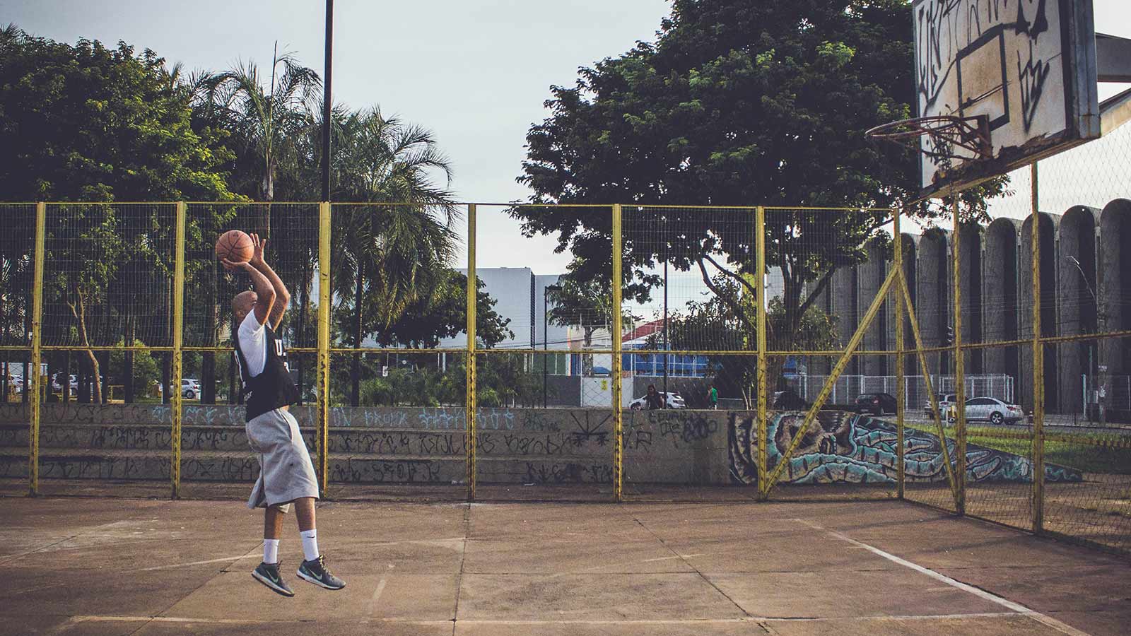A basketball player taking a jump shot on an outdoor court.