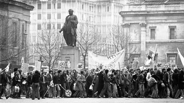 A large crowd protesting in front of a statue of a man.