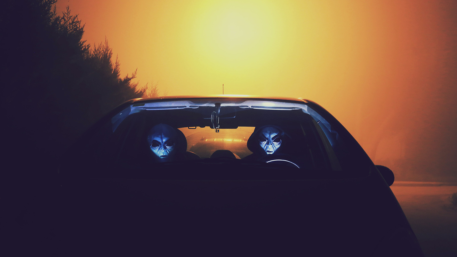 Two aliens sitting in a car with a sunset visible in the background.