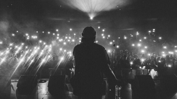 A from behind view of a rapper performing on stage in front of a large crowd.