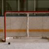 An ice hockey net with a puck sitting next to it.