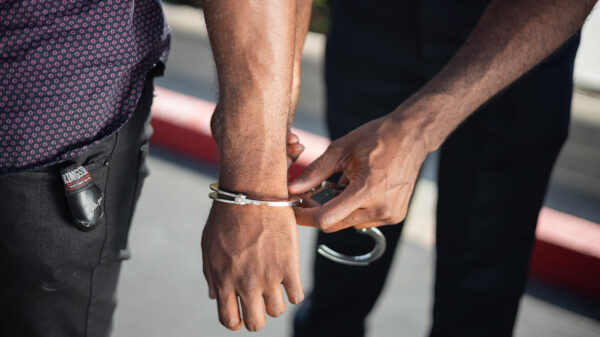 A police officer handcuffs a Black male.