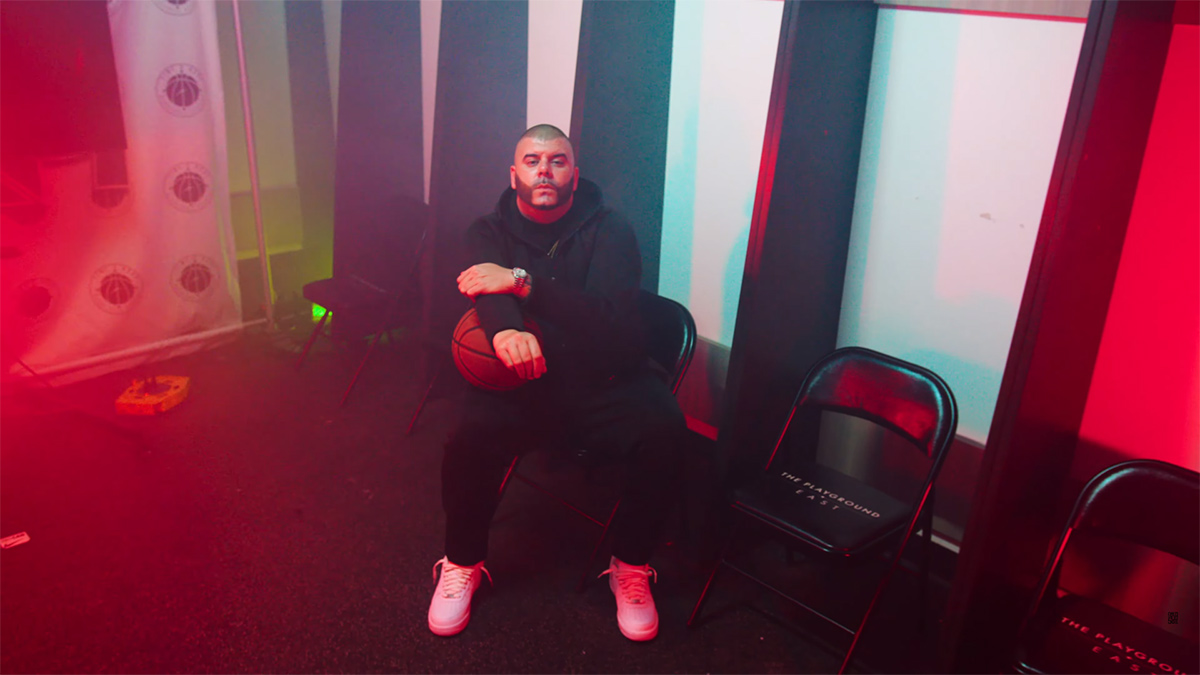 Rapper Peter Jackson holds a basketball while sitting on a stool in a scene from the Be Like Michael music video.