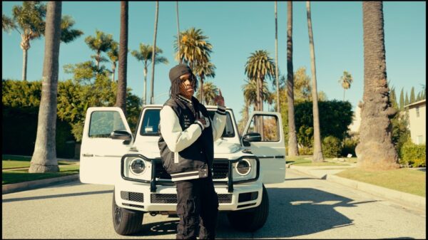TwoTiime stands in front of a luxury car under palm trees in a scene from the One More Chance music video.