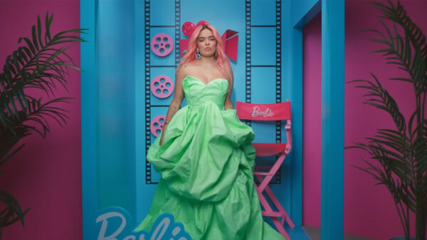 A woman in a green dress stands in front of a movie director's chair.
