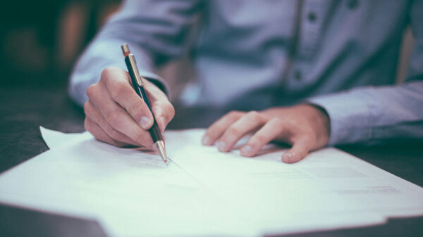 A hand holding a pen and writing on a piece of white paper.