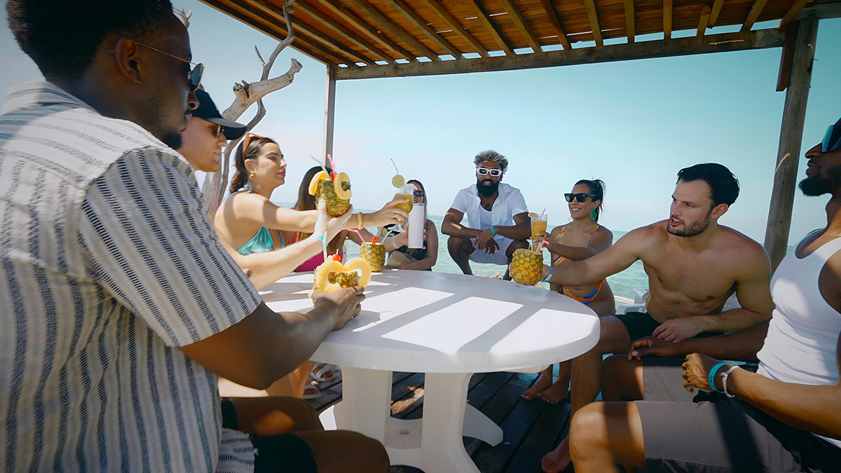 A group of people sit around a table under a tent on a beach
