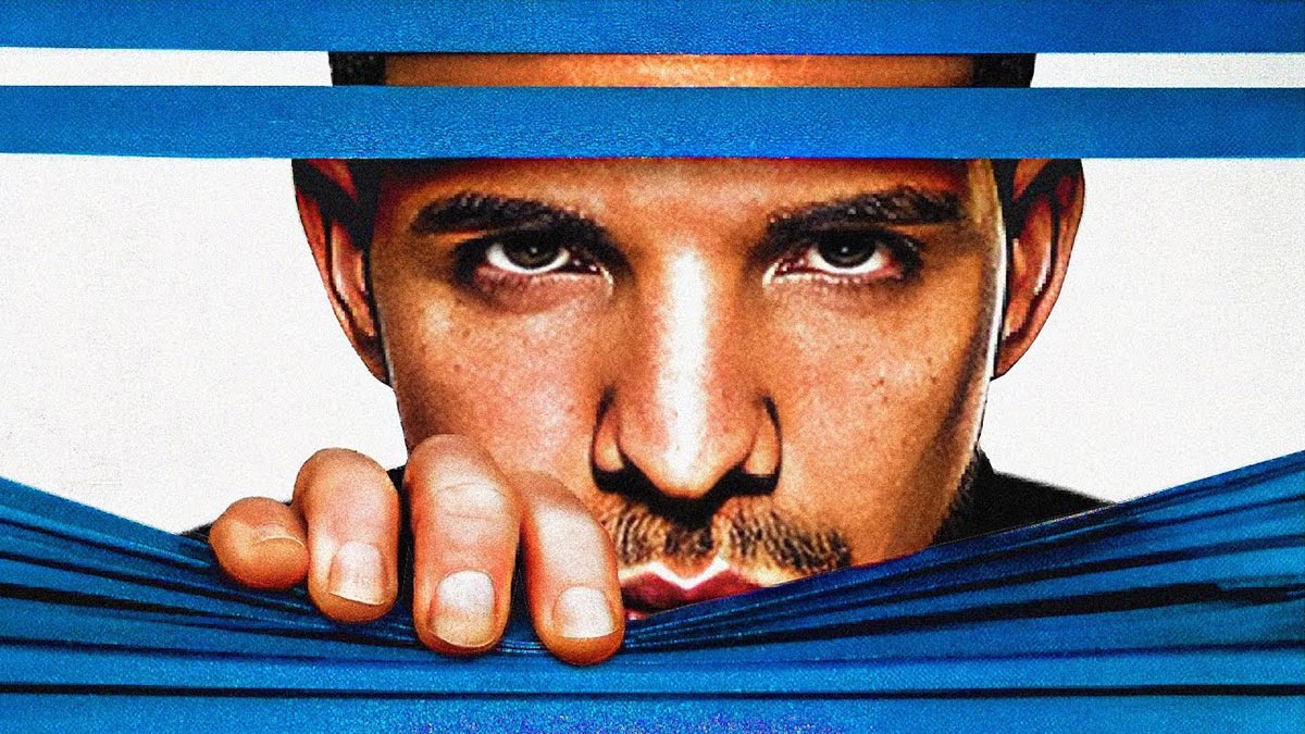 Drake pulling down blinds to look out a window.