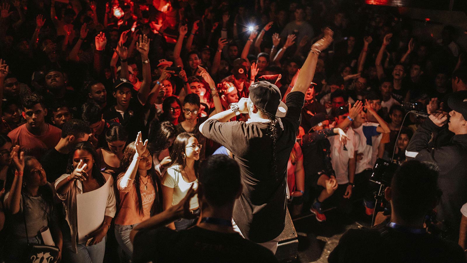 A from behind view of a rapper performing on stage in front of a large crowd.