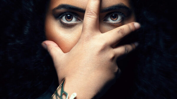 A woman holds her hand in front of her face with only her eyes showing.