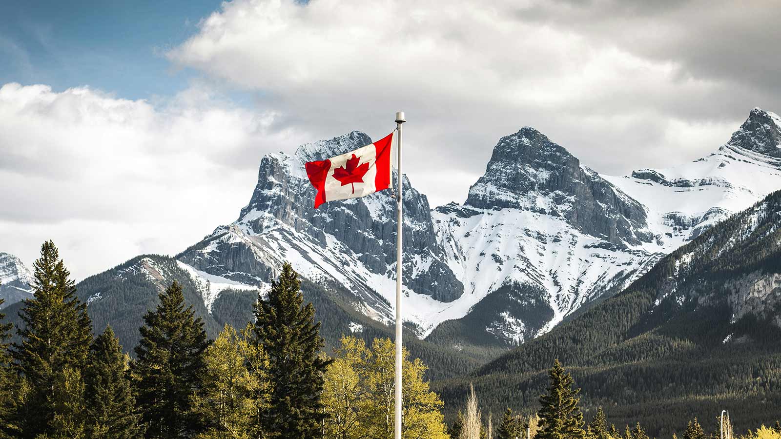 A Canadian flag with a snow covered mountain range in the background.