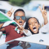 Two kids waving the flag of Sudan and throwing up peace signs.