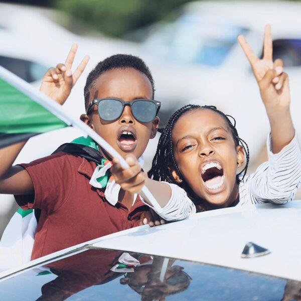 Two kids waving the flag of Sudan and throwing up peace signs.